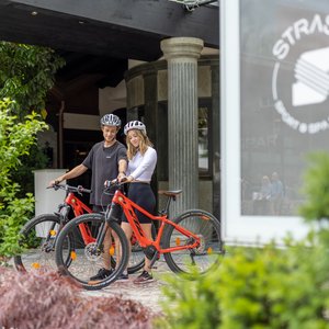 Vorbereitung zur Radtour Zwei Personen mit Helmen stehen mit ihren Mountainbikes vor einem Hotel, bereit für eine Fahrradtour.