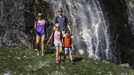 Familienwanderung am Wasserfall Familie wandert vor einem Wasserfall entlang eines Bergpfades in alpiner Landschaft.